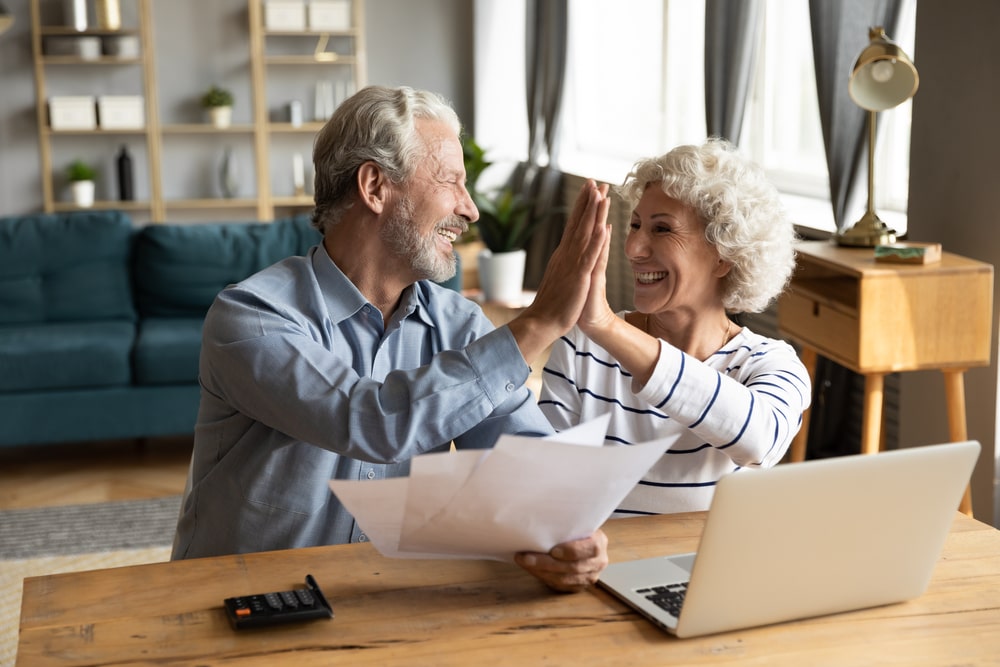 elderly couple high fiving over documents and computer